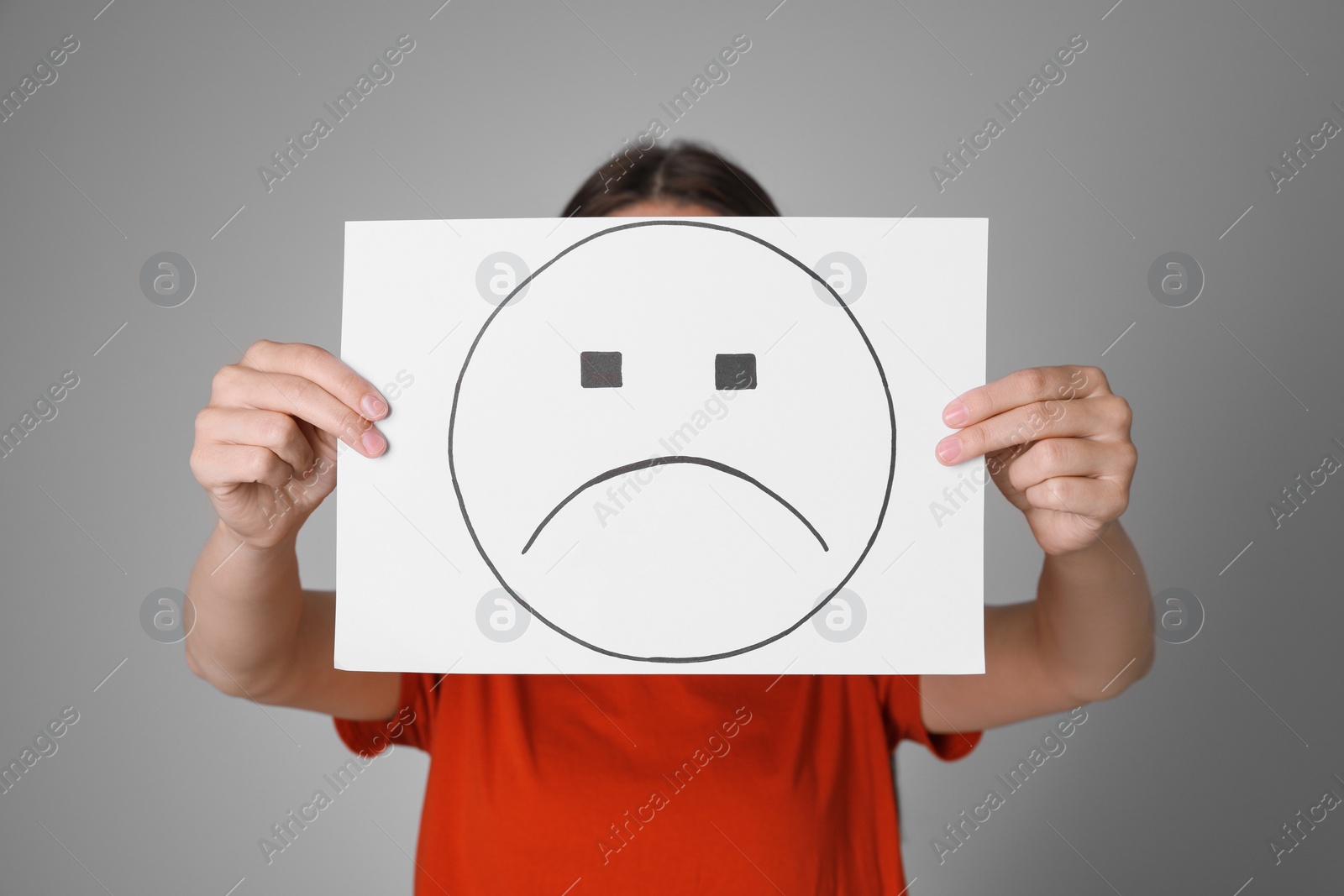 Image of Woman hiding behind sheet of paper with sad face on grey background