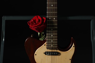Photo of Beautiful rose near electric guitar on black background
