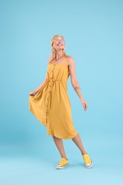 Portrait of smiling hippie woman dancing on light blue background