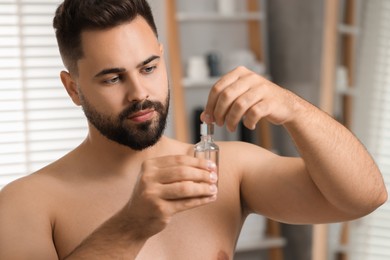Photo of Handsome man with cosmetic serum in his hands in bathroom