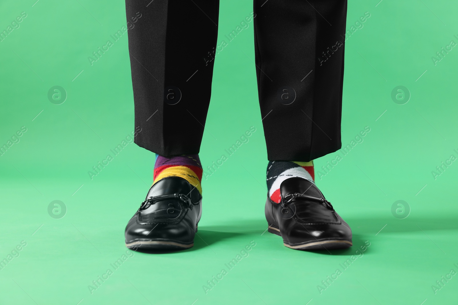 Photo of Man in different colorful socks, shoes and pants on light green background, closeup