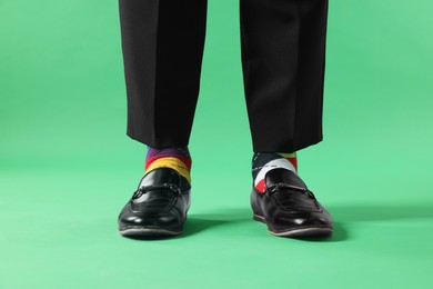 Photo of Man in different colorful socks, shoes and pants on light green background, closeup