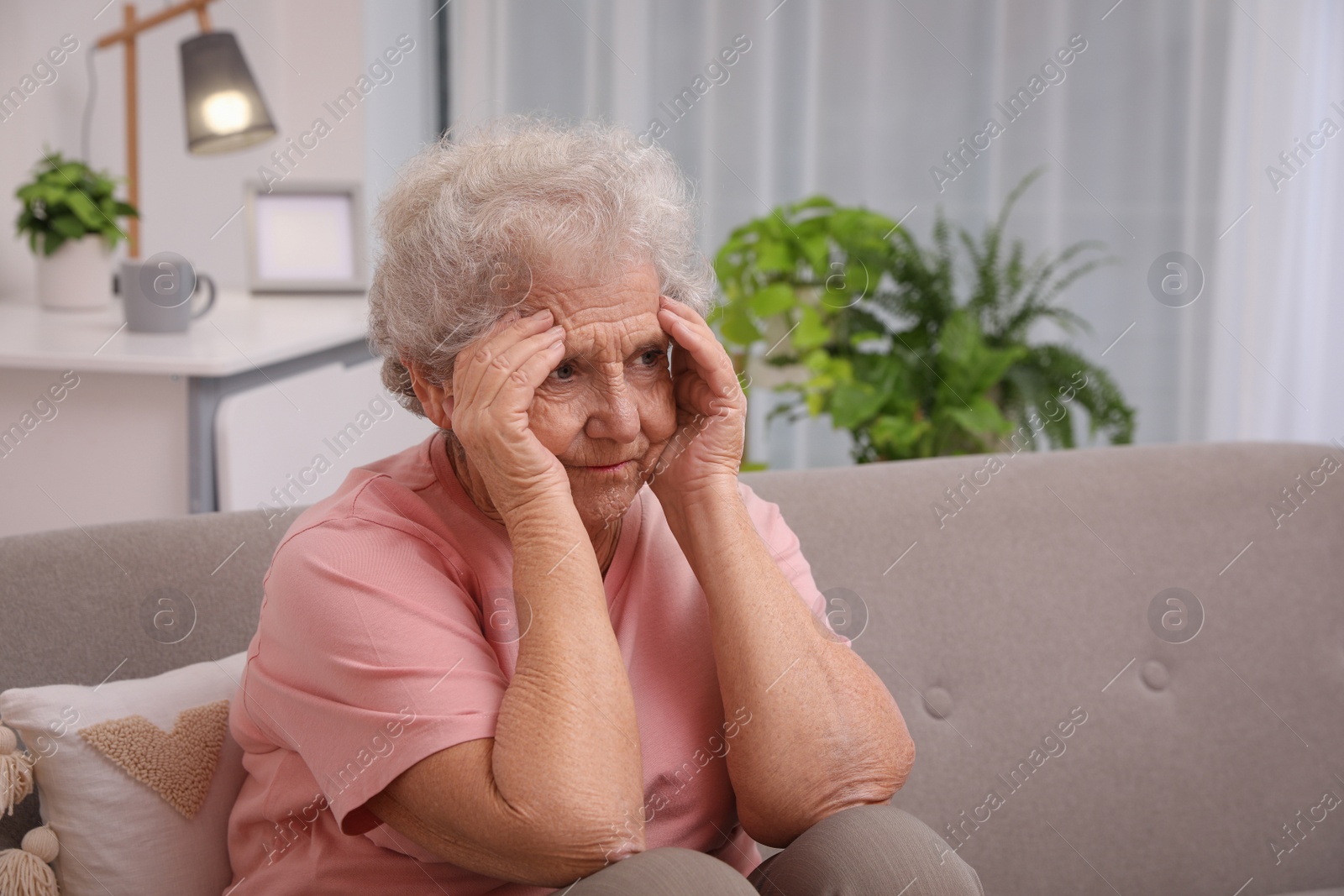 Photo of Senior woman with headache sitting on sofa at home