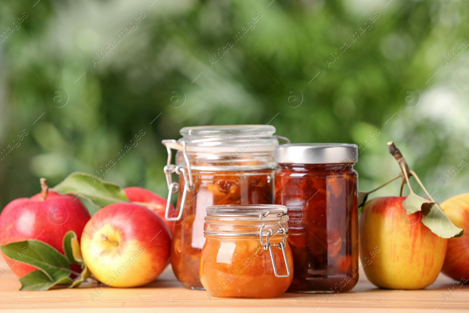 Photo of Delicious apple jams and fresh fruits on wooden table