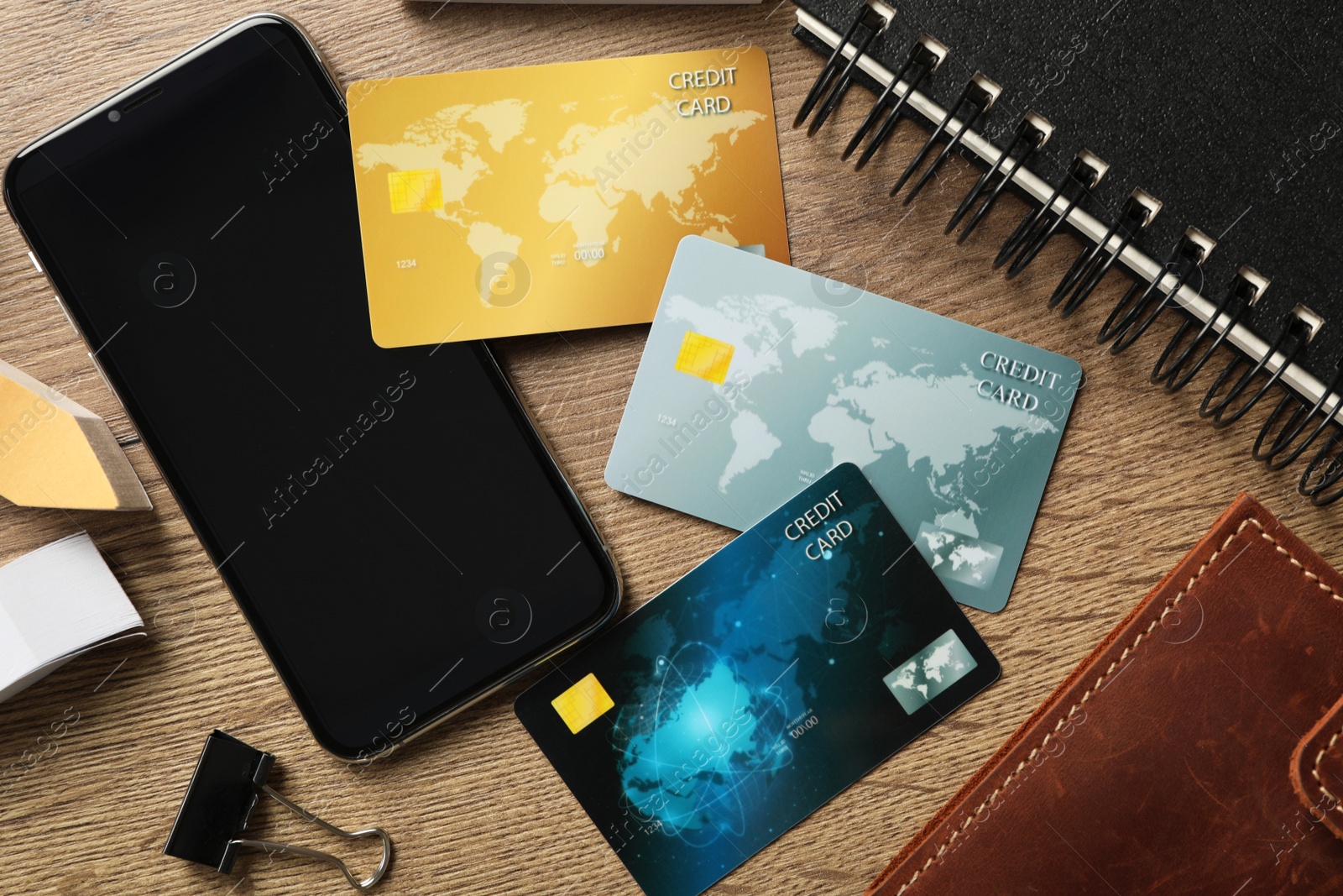 Photo of Different credit cards, smartphone and stationery on wooden table, flat lay. Space for design