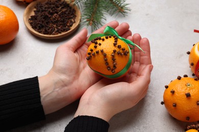 Photo of Woman holding pomander ball with green ribbon made of fresh tangerine and cloves at grey table, closeup