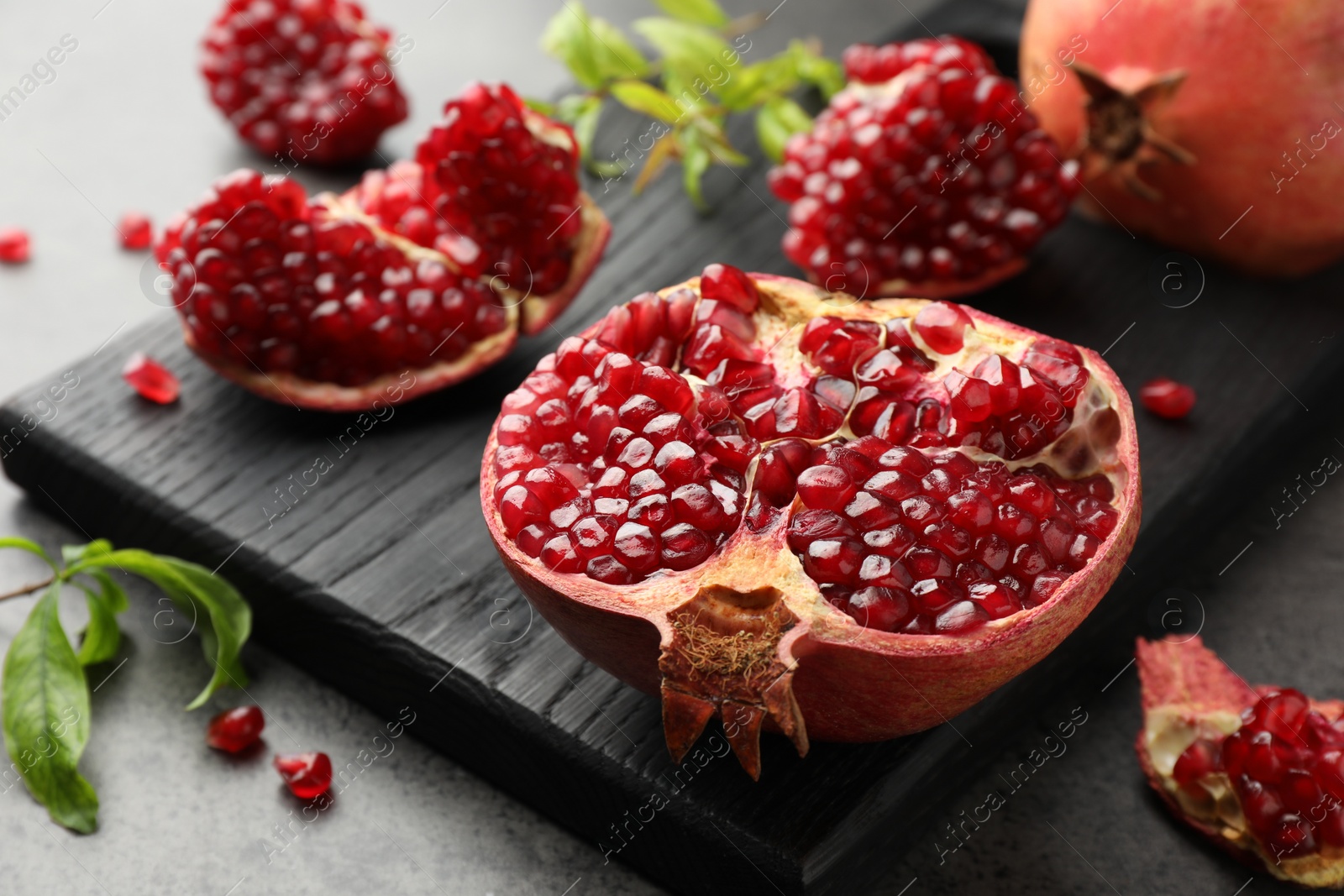 Photo of Cut fresh pomegranate and green leaves on grey table, closeup