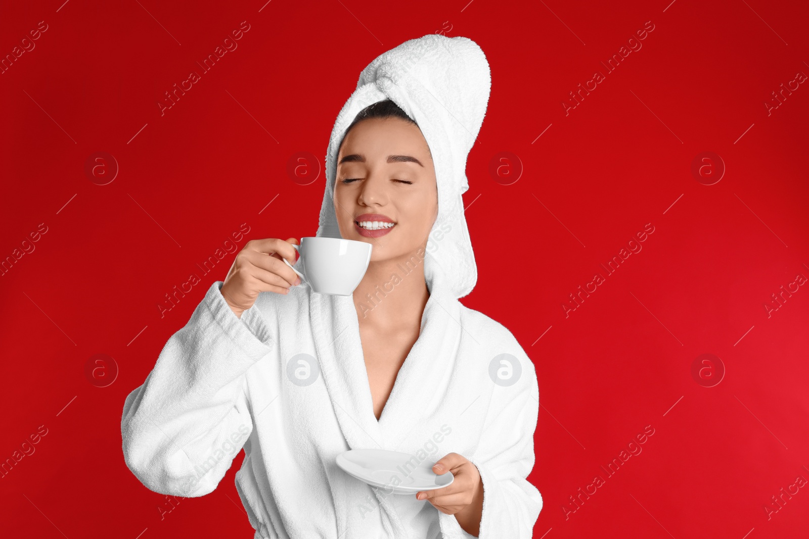 Photo of Young woman in bathrobe with cup of coffee on red background