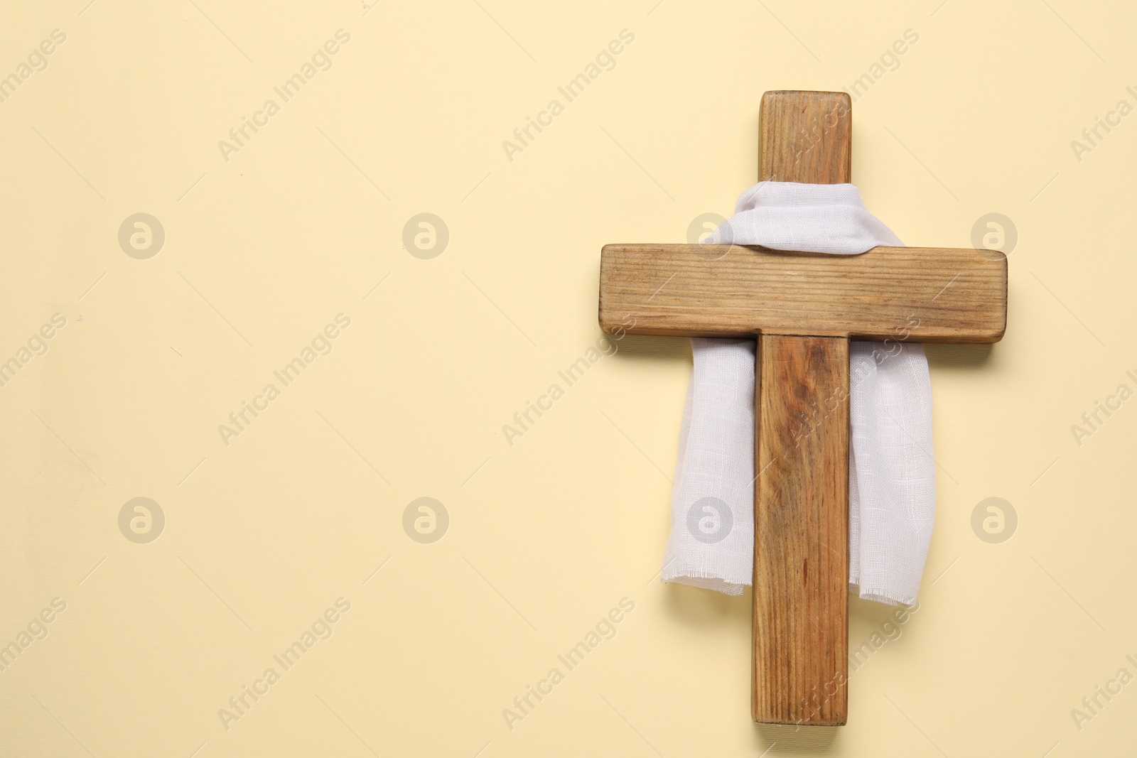 Photo of Wooden cross and white cloth on beige background, top view with space for text. Easter attributes