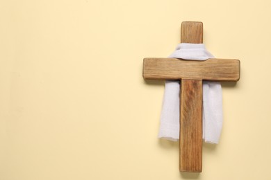 Photo of Wooden cross and white cloth on beige background, top view with space for text. Easter attributes