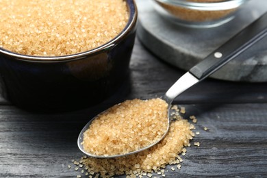 Photo of Brown sugar in bowl and spoon on black wooden table, closeup