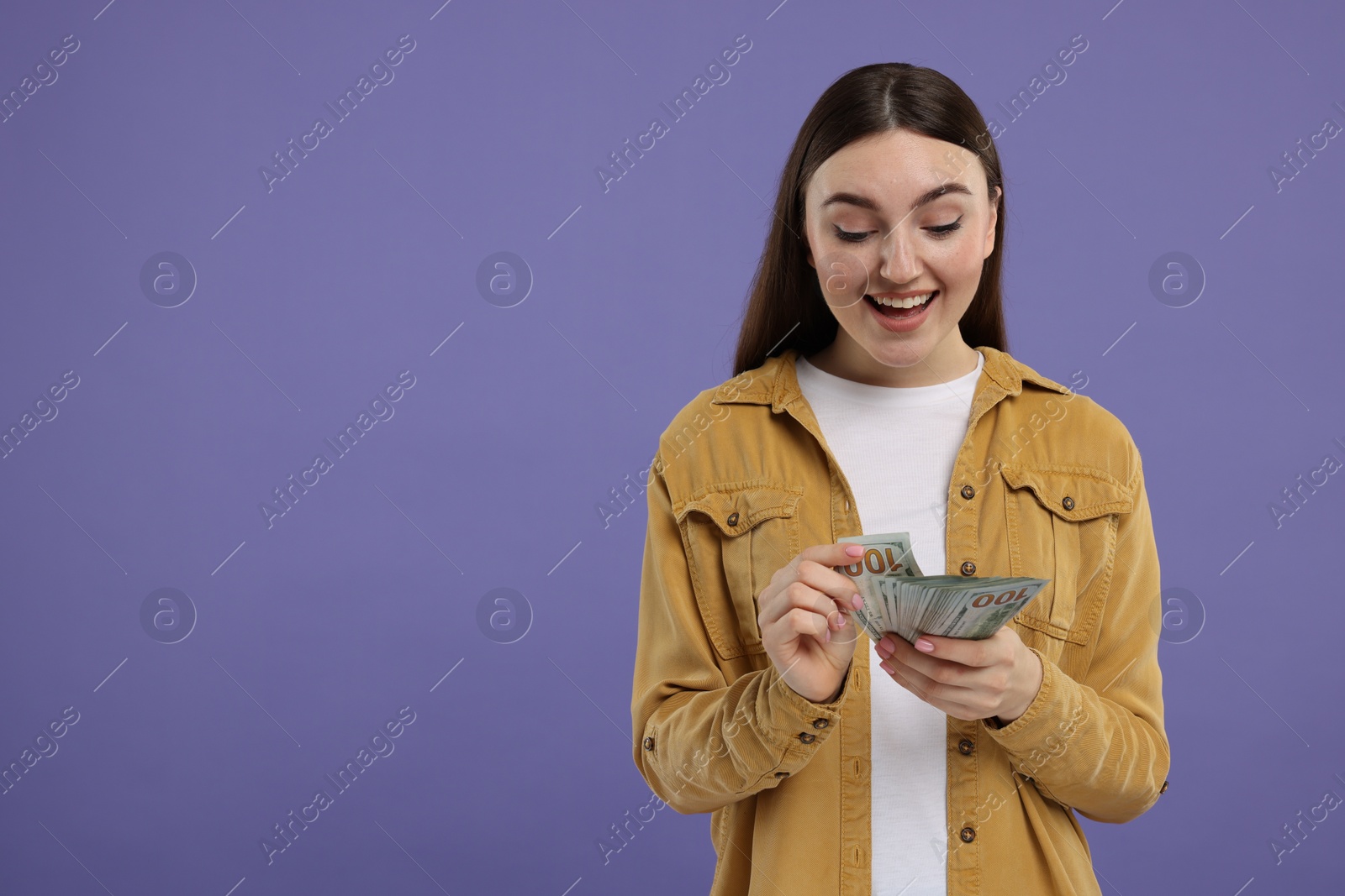 Photo of Happy woman with dollar banknotes on purple background, space for text