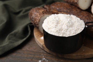 Photo of Scoop with cassava flour and roots on wooden table, closeup. Space for text