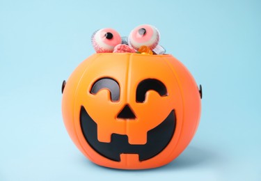 Photo of Halloween trick or treat bucket with different sweets on light blue