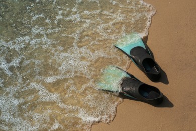Photo of Pair of turquoise flippers on sand near sea. Space for text