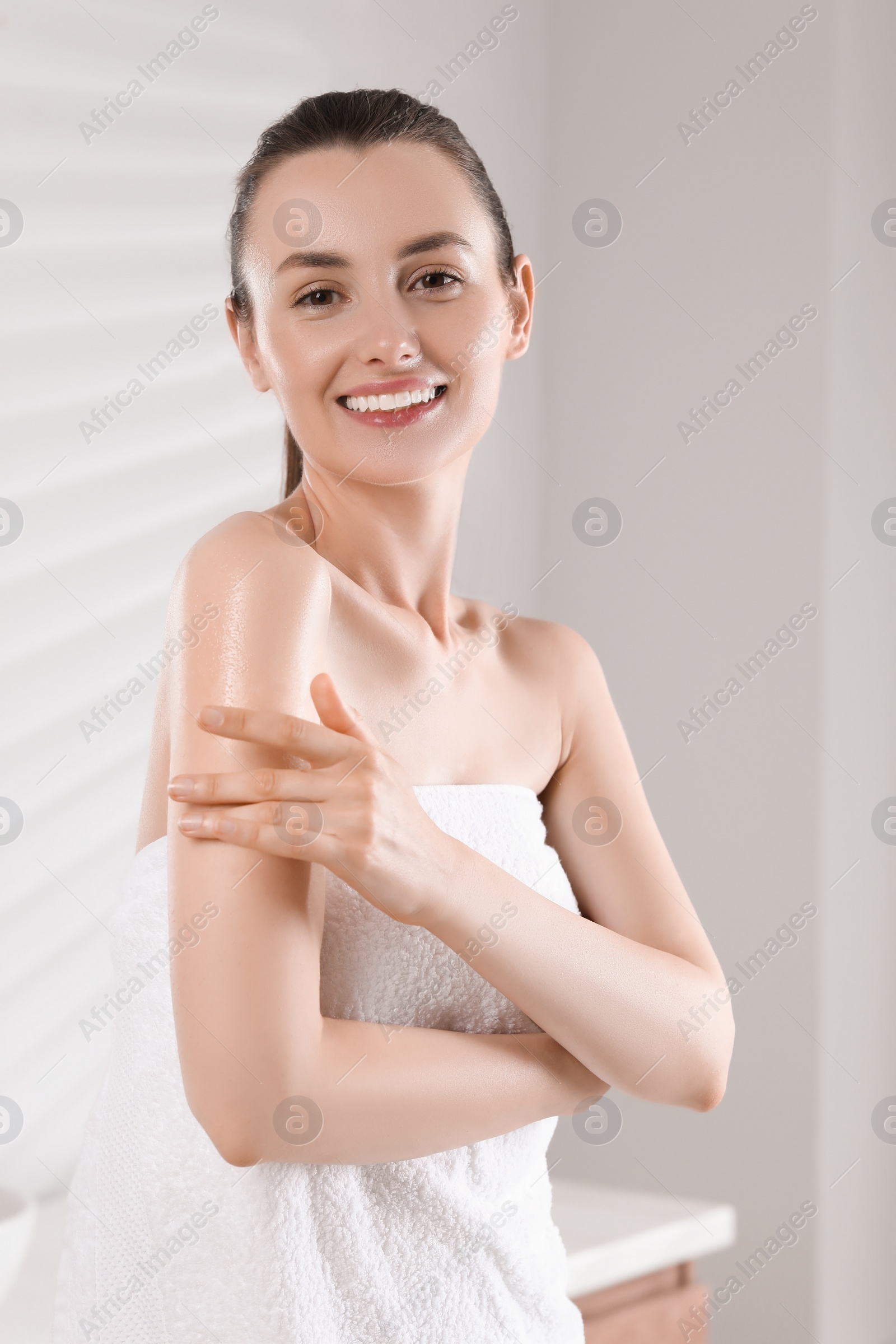 Photo of Happy woman applying body oil onto arm in bathroom