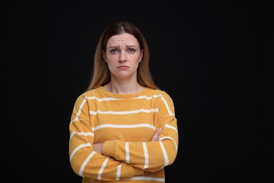 Portrait of sad woman with crossed arms on black background