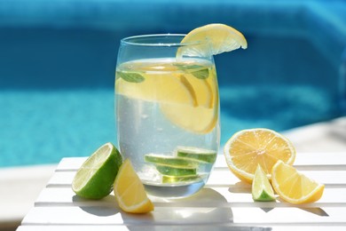 Photo of Refreshing water with lemon slices and mint on white wooden table near swimming pool, closeup