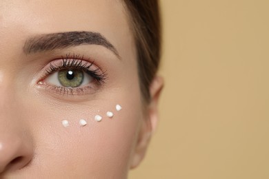 Photo of Young woman with cream around eye on beige background, closeup. Space for text