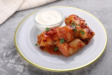 Photo of Delicious stuffed cabbage rolls served with sour cream on grey textured table, closeup
