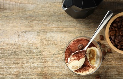 Delicious tiramisu in glass, spoon and coffee beans on wooden table, top view. Space for text