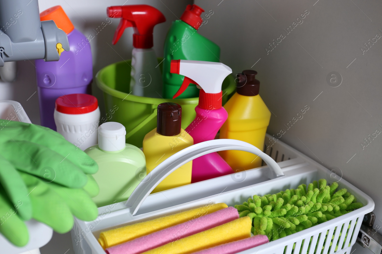 Photo of Open under sink cabinet with different cleaning supplies in kitchen, closeup