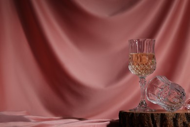 Photo of Glass of tasty alcoholic drink and empty one on wooden podium against color fabric, space for text