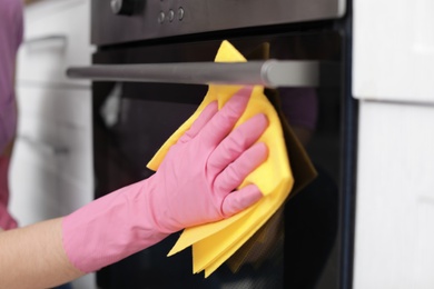 Photo of Woman cleaning oven with rag in kitchen, closeup