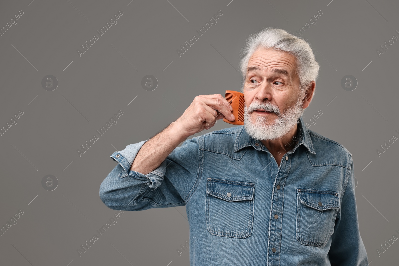 Photo of Senior man combing beard on grey background, space for text