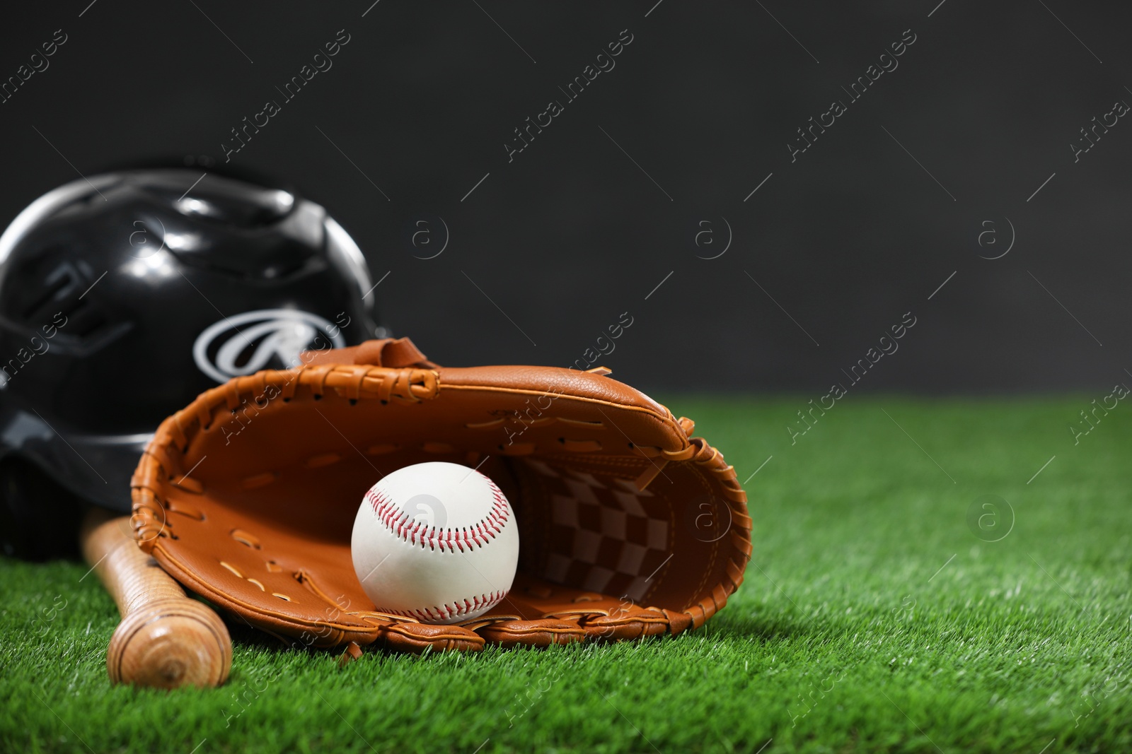 Photo of Baseball bat, batting helmet, leather glove and ball on green grass against dark background. Space for text