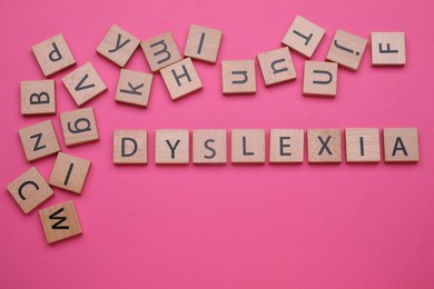 Photo of Wooden cubes with word Dyslexia on pink background, flat lay