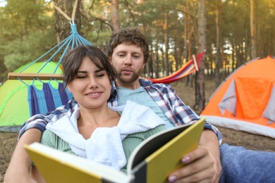 Lovely couple with book resting in comfortable hammock outdoors