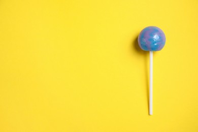 Stick with bright lollipop on yellow background, top view. Space for text