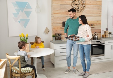 Photo of Parents treating kids with oven baked cookies in kitchen