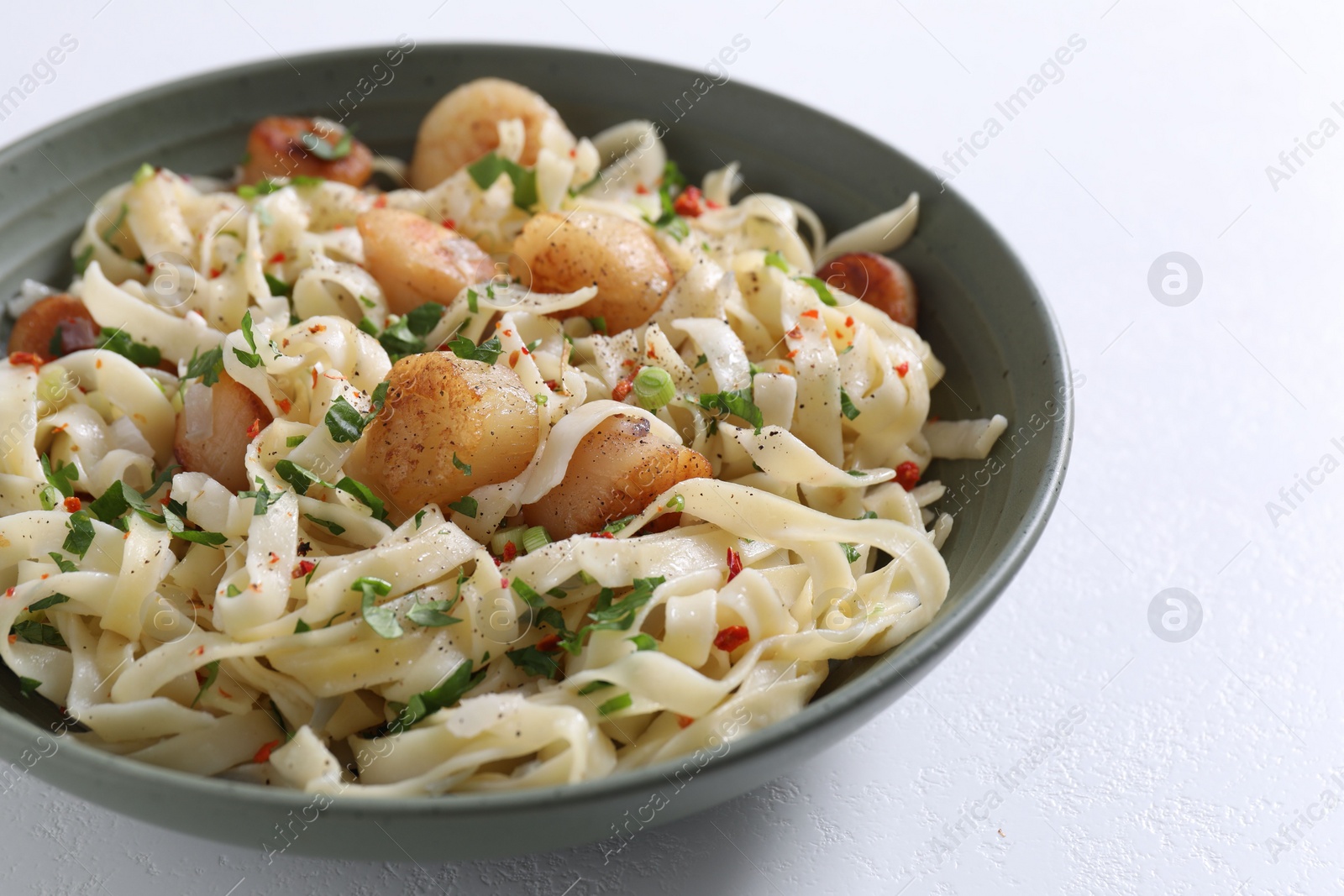 Photo of Delicious scallop pasta with spices in bowl on white table, closeup