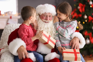 Little children with gift boxes sitting on authentic Santa Claus' knees indoors