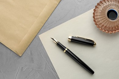 Photo of Stylish fountain pen, inkwell, envelope and paper on grey textured table, flat lay