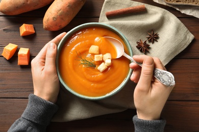 Photo of Woman eating tasty sweet potato soup at table, top view