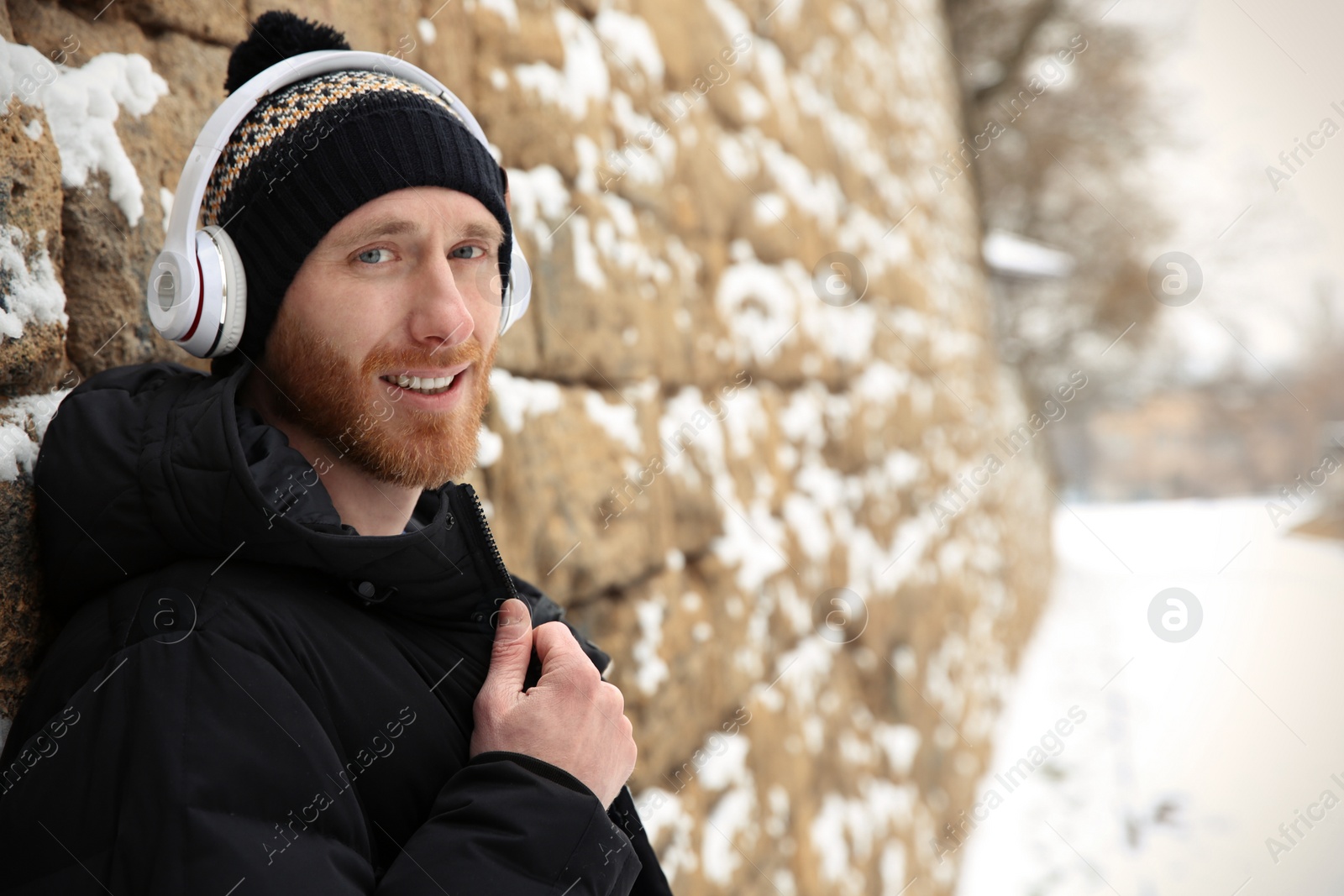 Photo of Young man listening to music with headphones near stone wall. Space for text