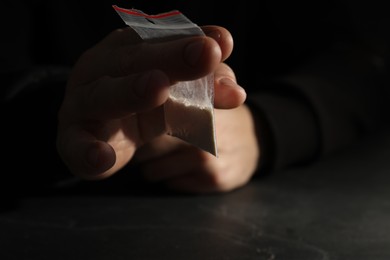 Drug addiction. Man with plastic bag of cocaine at grey table, selective focus
