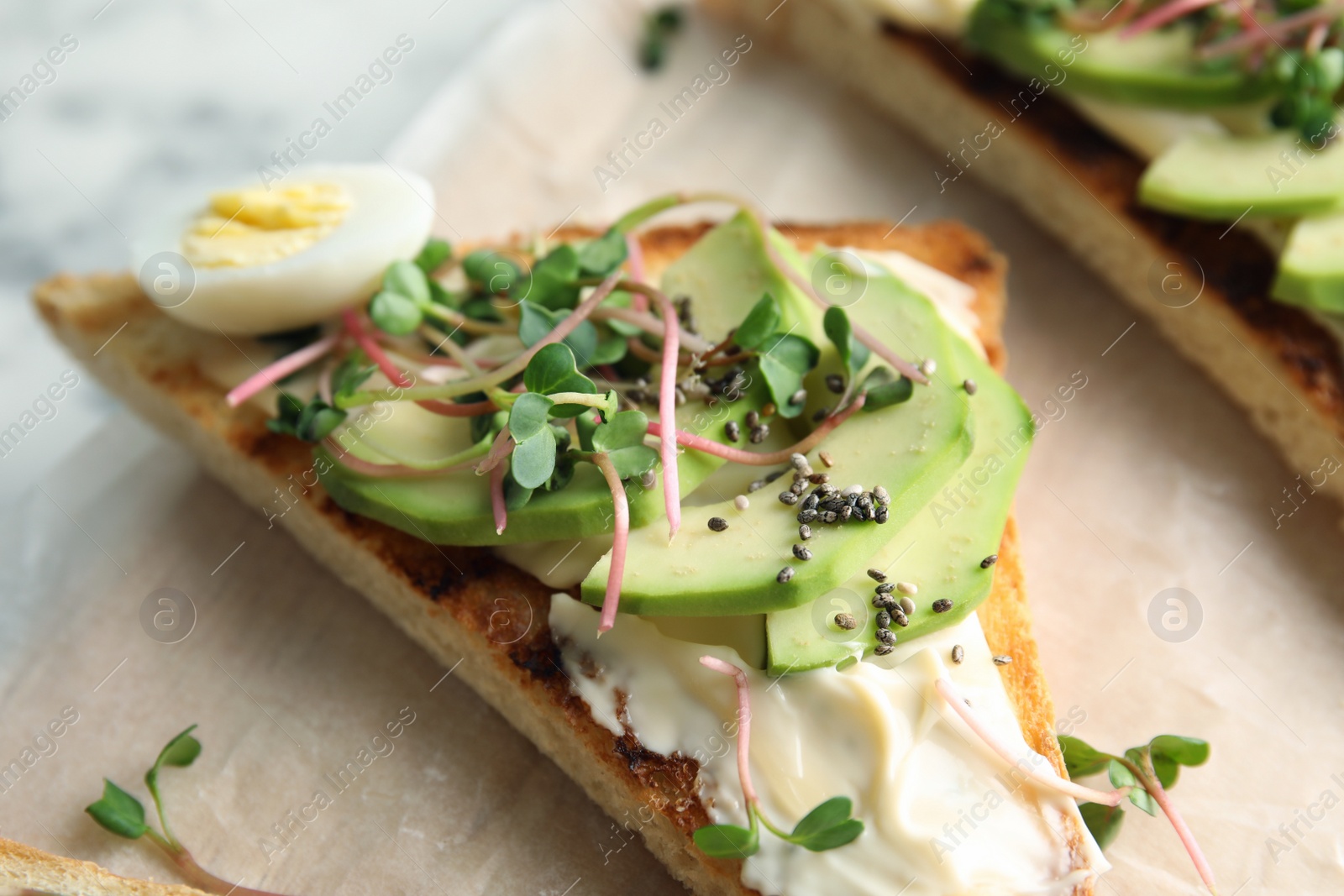 Photo of Tasty toast with avocado, sprouts and chia seeds on parchment, closeup