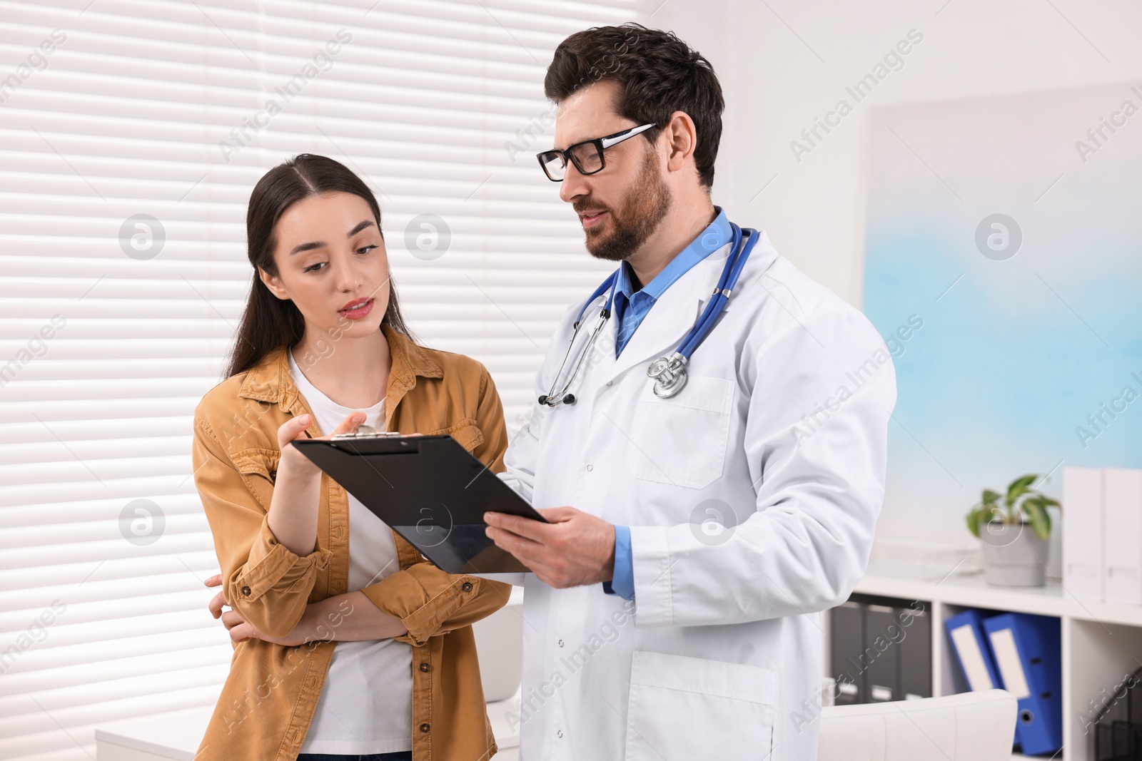 Photo of Doctor with clipboard consulting patient during appointment in clinic