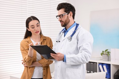 Doctor with clipboard consulting patient during appointment in clinic