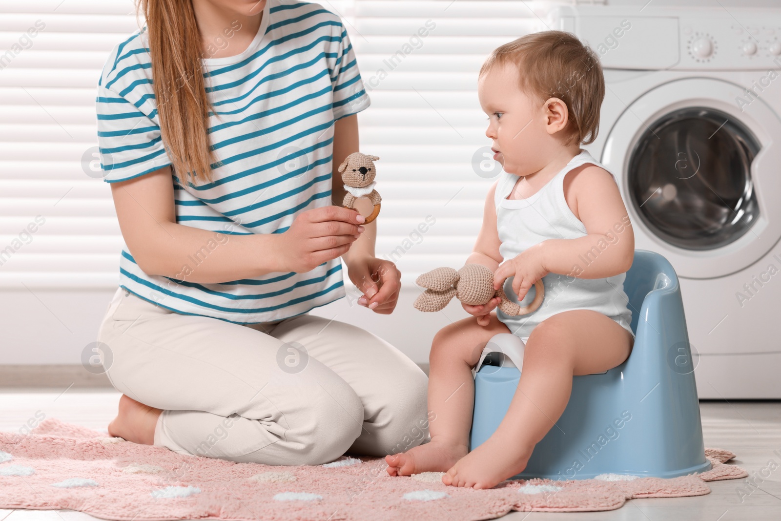 Photo of Mother training her child to sit on baby potty indoors