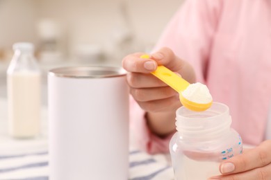 Photo of Woman preparing infant formula at table indoors, closeup. Baby milk