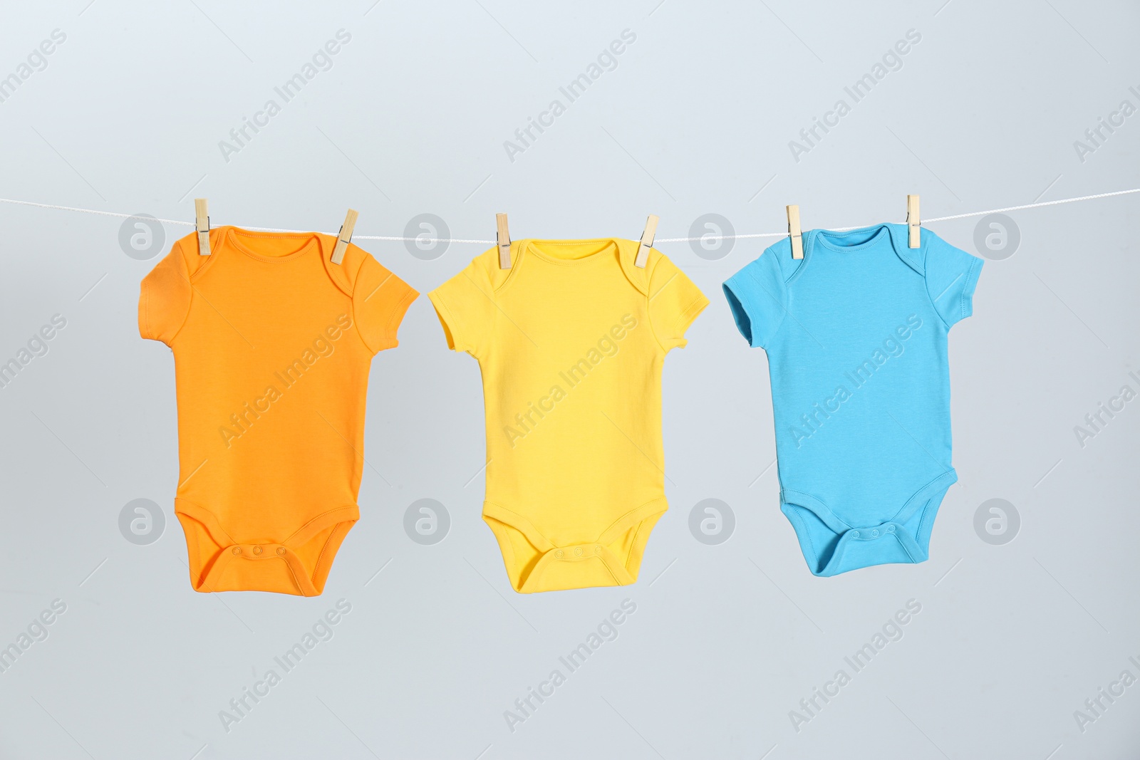 Photo of Different baby onesies hanging on clothes line against light grey background. Laundry day