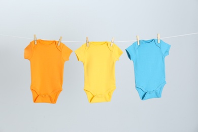 Different baby onesies hanging on clothes line against light grey background. Laundry day