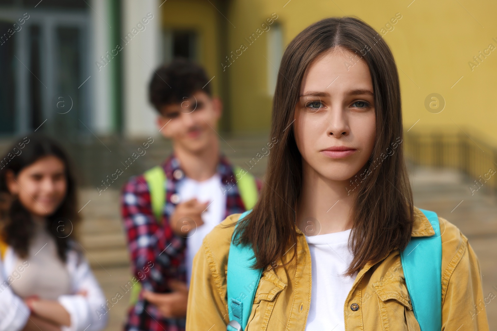 Photo of Teen problems. Lonely girl standing separately from other students outdoors