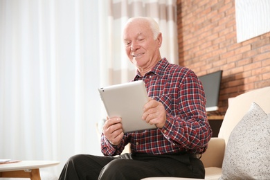 Elderly man using tablet PC on sofa in living room