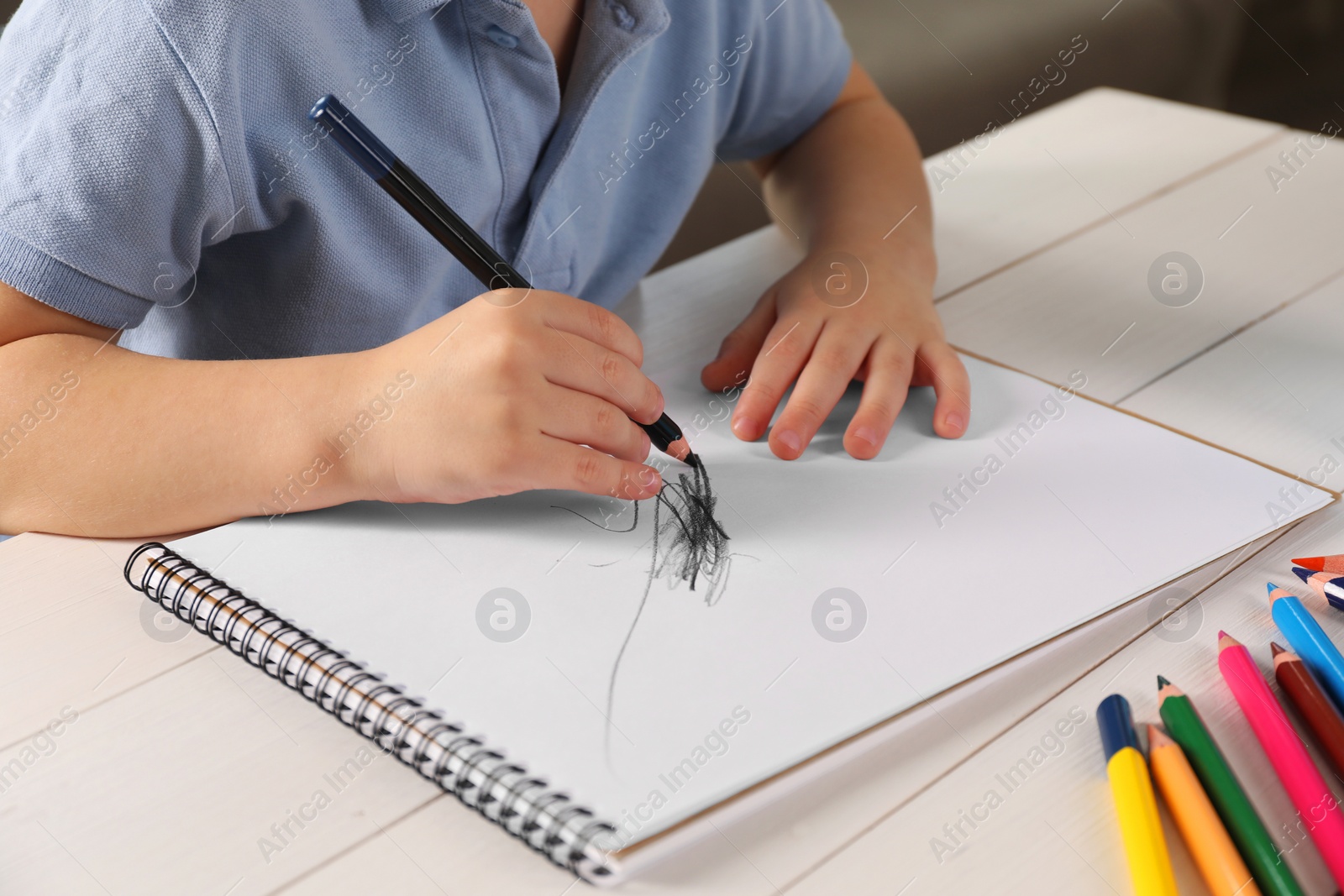 Photo of Little boy drawing with pencil at white wooden table indoors, closeup. Child`s art